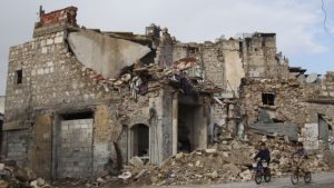 Syrian boys bike past a building in Aleppo which has fallen to ruins after years of civil war. Photo by Hosam Katan from Creative Commons.