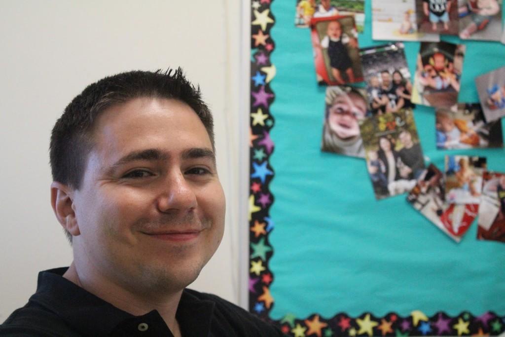Mr. Schuler poses in his classroom in front of pictures of his son. Photo by Amurri Davis.